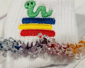 May include: White knitted sock with a green snake and rainbow stripes embroidered on the front. The sock has a rainbow colored beaded trim.