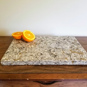 May include: A rectangular, gray and white marble cutting board with a swirl pattern. Two halves of an orange are on the board.