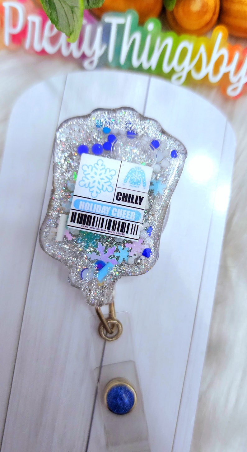 May include: A silver glitter resin keychain with a blue snowflake, a blue sweater, and the text "CHILLY HOLIDAY CHEER".
