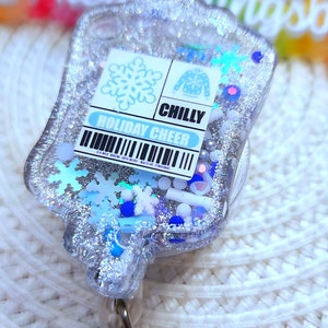 May include: A silver glitter badge holder with a blue and white snowflake design. The badge holder has a clear plastic front and a silver metal clip. The text "Holiday Cheer" and "Chilly" are printed on the badge holder.
