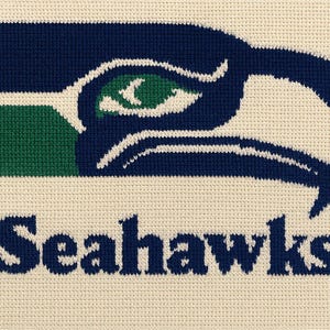 Puede incluir: Primer plano de un diseño bordado en azul y verde de la cabeza de un pájaro con la palabra "Seahawks" bordada debajo.