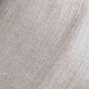 K&ouml;nnte beinhalten: Nahaufnahme eines hellbeigen Leinenstoffs. Der Stoff hat ein strukturiertes Aussehen mit sichtbarem Gewebe und subtilen Farbvariationen. Das Material wirkt weich und leicht zerknittert, was auf eine nat&uuml;rliche Textilfaser hindeutet.
