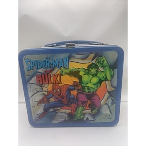 May include: Blue metal lunchbox featuring Spider-Man and the Hulk. The lunchbox has a handle and a clasp closure. The front of the lunchbox has a graphic of Spider-Man and the Hulk with the text "Spider-Man and the Hulk!"