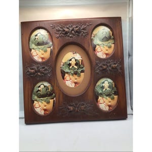 May include: A wooden picture frame with an oval center and four smaller oval openings. Each opening contains a relief sculpture of a figure in a garden setting. The frame is a dark brown color with floral carvings.