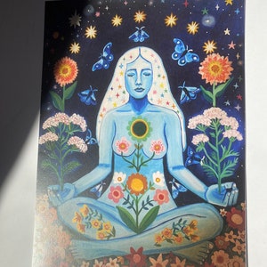 May include: A blue figure sits in a meditative pose surrounded by flowers and stars. The figure has a flower growing from their chest and is surrounded by butterflies and stars.