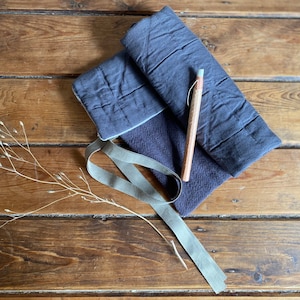 Puede incluir: Una bolsa de tela acolchada azul con un lápiz de madera marrón y una cinta gris sobre una superficie de madera.