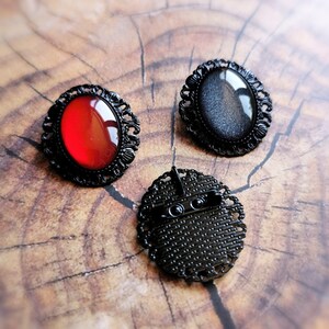 May include: Three black metal brooches with different colored glass insets. The brooches have an ornate design and are perfect for adding a touch of vintage style to any outfit.