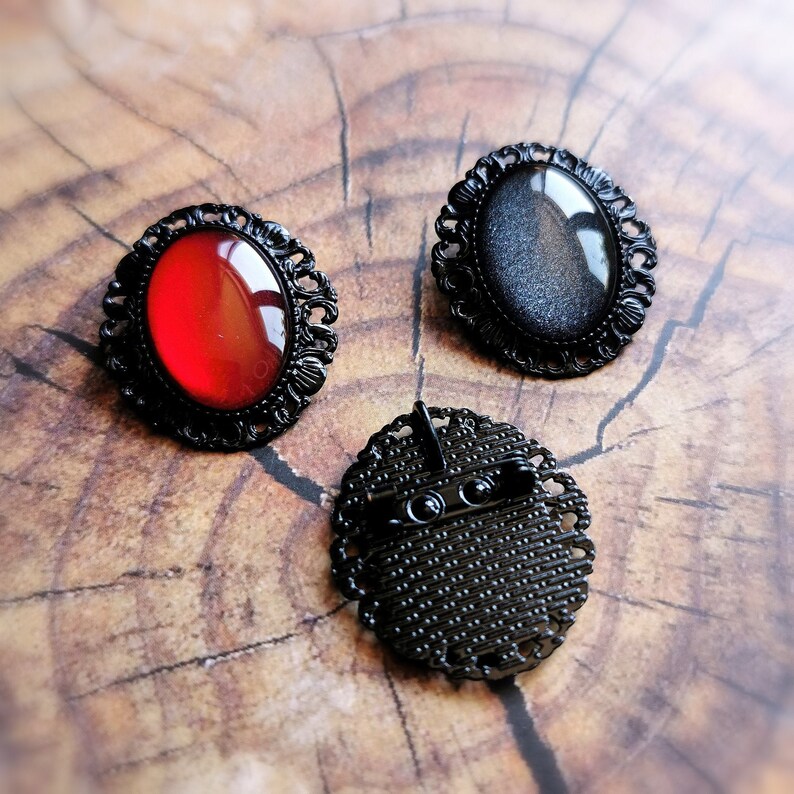 May include: Three black metal brooches with different colored glass insets. The brooches have an ornate design and are perfect for adding a touch of vintage style to any outfit.