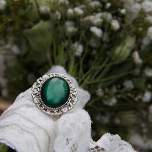 May include: A white lace ribbon tied around a bouquet of white baby's breath flowers with a silver ring featuring a green gemstone.