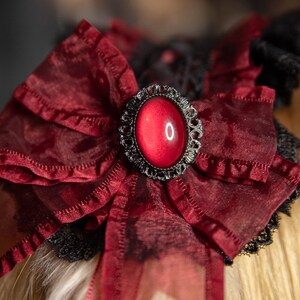 May include: A red velvet bow with a black lace trim and a large, red, jewel-toned button in the center.