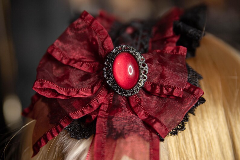 May include: A red velvet bow with a black lace trim and a large, red, jewel-toned button in the center.