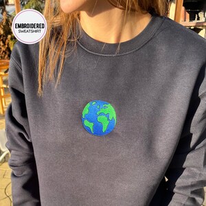 May include: Black sweatshirt with an embroidered green and blue globe design. The sweatshirt is a crew neck style.