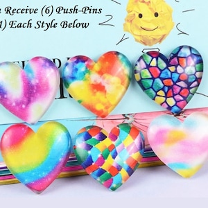 May include: Six heart-shaped push pins with colorful designs. The pins feature various patterns, including tie-dye, stained glass, and a galaxy theme. The text "You Receive (6) Push-Pins (1) Each Style Below" is visible.