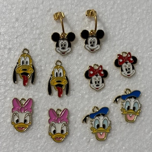 May include: Gold-plated interchangeable earrings with ten Disney character charms. The charms include Mickey Mouse, Minnie Mouse, Pluto, Donald Duck, and Daisy Duck. The text "DISNEY GANG" is at the top.