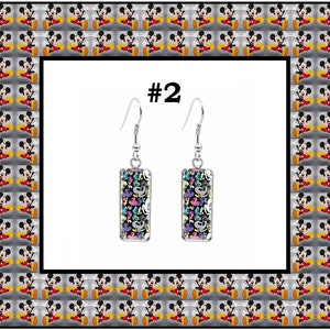 Peut inclure: Une paire de boucles d'oreilles pendantes en argent avec des breloques rectangulaires en verre. Les breloques pr&eacute;sentent un motif color&eacute; de t&ecirc;tes et de mains de Mickey Mouse. Les boucles d'oreilles sont &eacute;tiquet&eacute;es #2.