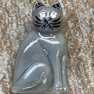May include: A grey glass cat figurine with black painted details and rhinestone eyes.
