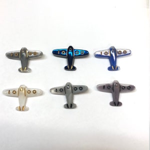 May include: Six plastic airplane buttons in various colors, including white, gray, blue, and purple. The buttons have gold accents and are perfect for adding a whimsical touch to crafts and sewing projects.