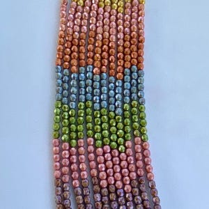 May include: A strand of iridescent glass beads in a rainbow of colours, including gold, pink, orange, blue, green, and purple. The beads are faceted and have a shimmery finish.
