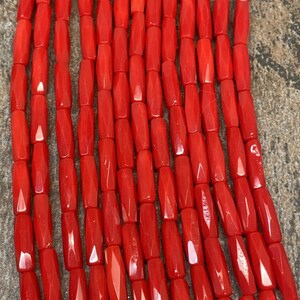 Könnte beinhalten: Eine Strähne aus leuchtend roten Korallenperlen, jede Perle ist facettiert und hat eine rechteckige Form.