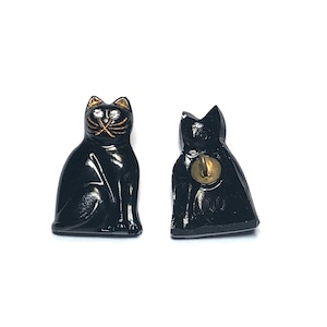 May include: Two black cat buttons with gold accents. The button on the left shows the cat sitting with its tail curled around its legs. The button on the right shows the back of the cat.