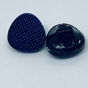 May include: Two oval-shaped buttons, one blue with a textured surface and one black with a white rim.
