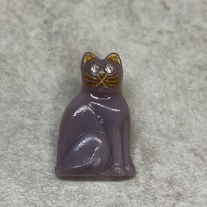 May include: A purple glass cat figurine with gold accents and rhinestone eyes. The cat is sitting with its tail curled around its legs.
