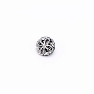 May include: A silver button with a decorative, intricate design. The button is circular and has a raised, textured pattern.