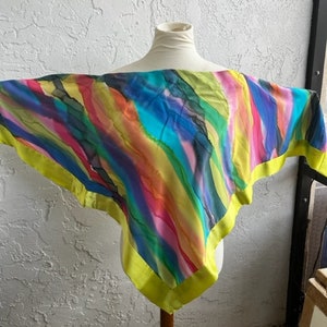 May include: A colorful silk scarf with a yellow border. The scarf features a watercolor-like design with stripes of blue, green, pink, orange, and purple.