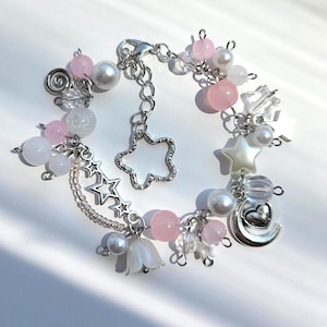 May include: A delicate bracelet featuring a mix of pink, white, and clear beads. The bracelet includes pearl accents, star and moon charms, and a silver-toned chain with a star-shaped pendant. The design is feminine and whimsical.