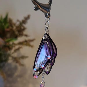 May include: A silver heart-shaped keychain with a purple and white butterfly charm and a dangling purple crystal.
