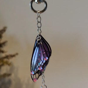 May include: A silver key chain with a purple butterfly charm and dangling purple beads.