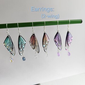 May include: Five pairs of fairy wing earrings with iridescent glitter. The wings are made of clear resin with black veins and are attached to silver hooks. The earrings are available in four colors: blue, pink, purple, and iridescent.