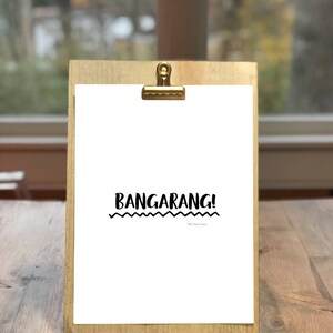 May include: A white printable sign with the text "Bangarang!" in black, with a wavy line underneath the text. The sign is on a wooden clipboard with a gold clip.