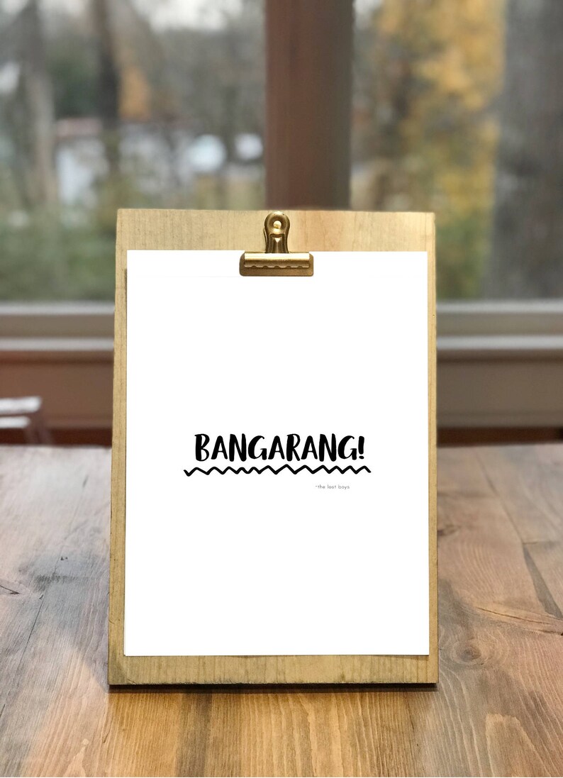 May include: A white printable sign with the text "Bangarang!" in black, with a wavy line underneath the text. The sign is on a wooden clipboard with a gold clip.