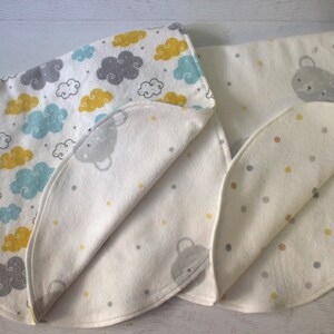May include: Two white baby blankets with different patterns. One blanket has a cloud and star pattern in blue, gray, and yellow. The other blanket has a polka dot pattern in gray and yellow.