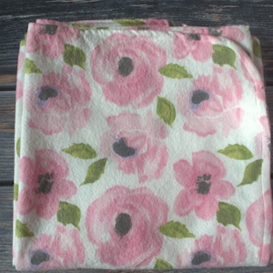 May include: A white fabric baby blanket with a pink floral pattern. The flowers are a watercolor style with green leaves.