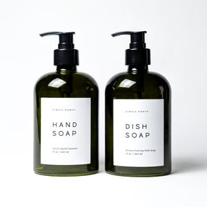 May include: Two dark green glass soap dispensers with black pumps. One label reads "HAND SOAP" and the other reads "DISH SOAP". Each bottle contains 15 oz / 445 ml of soap. The brand name "SIMPLE NORTH" is printed on each label.