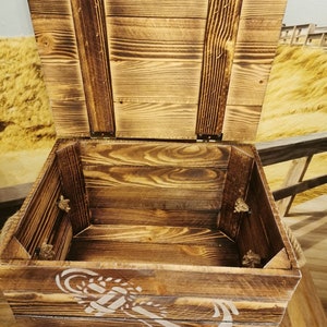 May include: A wooden storage box with a hinged lid and rope handles. The box is decorated with a white anchor design and has a distressed wood finish.