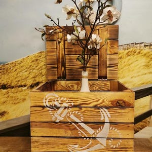 May include: A wooden storage box with a hinged lid and metal legs. The box is decorated with a white anchor design and has a distressed wood finish.