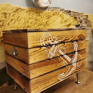 May include: Wooden storage box with a white anchor design and silver metal legs. The box has a distressed wood finish and a silver metal handle.