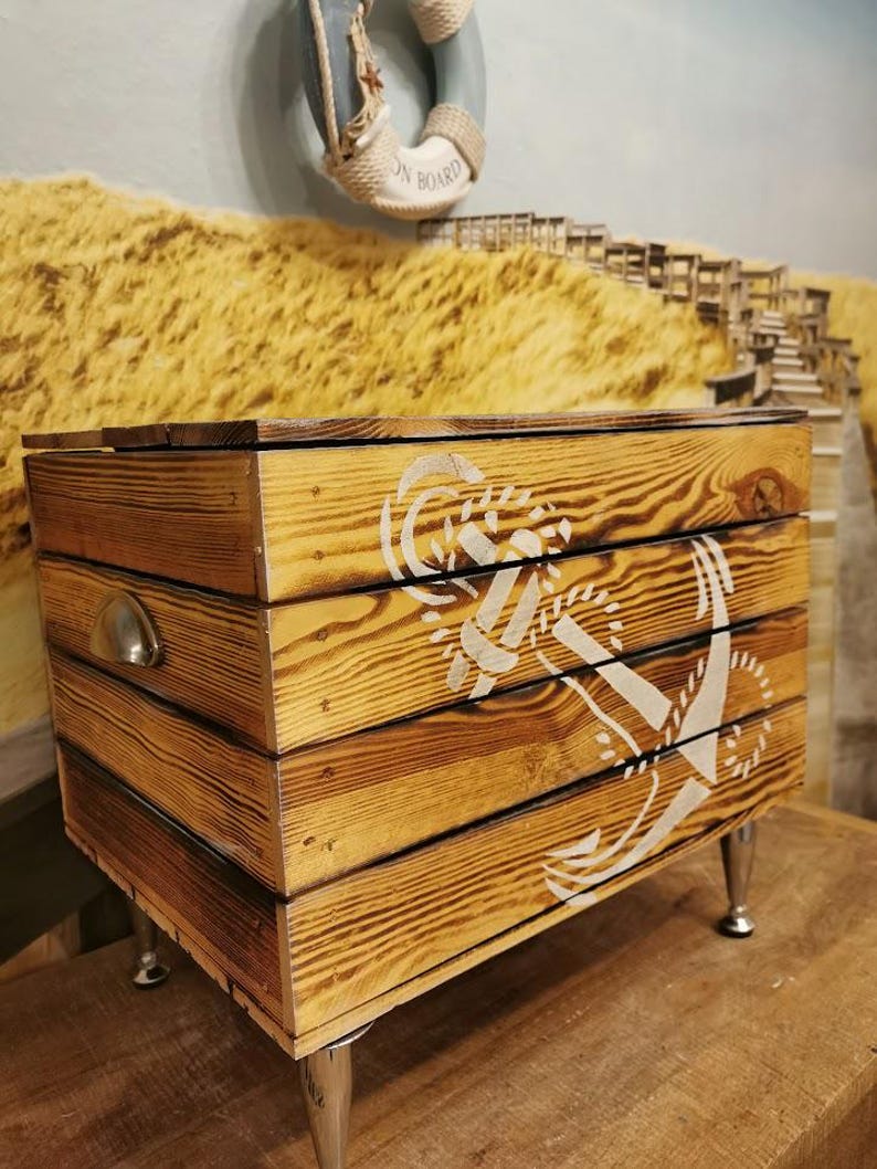 May include: Wooden storage box with a white anchor design and silver metal legs. The box has a distressed wood finish and a silver metal handle.