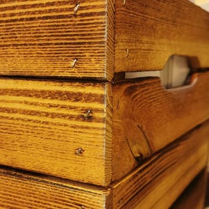 May include: A wooden crate with a natural brown stain. The crate is made of thick wood planks and has a rustic look. The crate has a handle on the side and is made of solid wood.