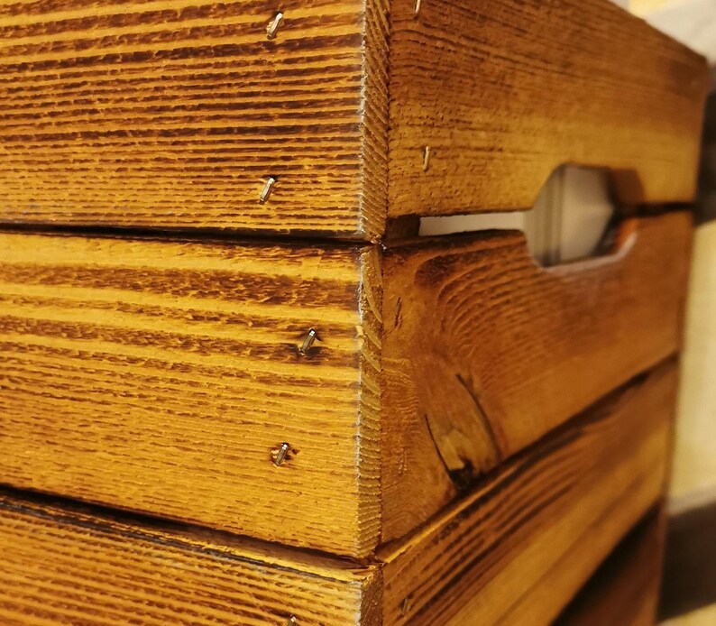May include: A wooden crate with a natural brown stain. The crate is made of thick wood planks and has a rustic look. The crate has a handle on the side and is made of solid wood.