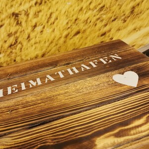 May include: A wooden sign with the words "HEIMATHAFEN" painted in white. A white heart is painted below the text.