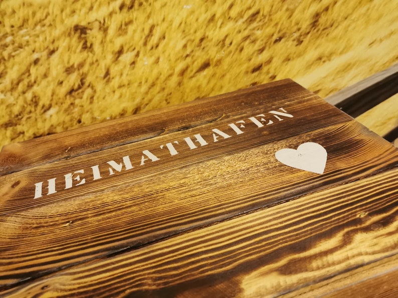 May include: A wooden sign with the words "HEIMATHAFEN" painted in white. A white heart is painted below the text.