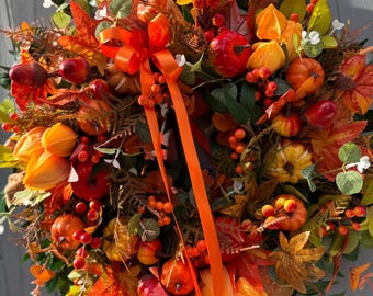 May include: A vibrant autumn wreath featuring a mix of fall foliage, including orange, red, and yellow leaves, small pumpkins, and berries. An orange ribbon is tied in a bow. The wreath is a festive decoration.