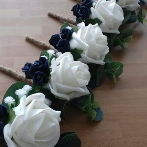 Op de afbeelding: Een set van zes witte en marineblauwe corsages met witte rozen, marineblauwe bloemen en groen.