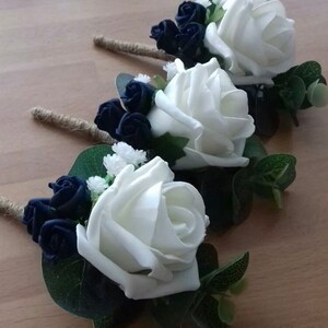 Op de afbeelding: Drie witte roos corsages met donkerblauwe rozen en groen.