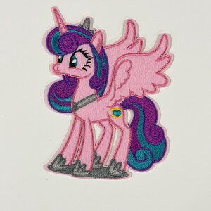 May include: An embroidered iron-on patch featuring a pink unicorn with wings, a purple and teal mane and tail, a silver horn, and a small heart-shaped emblem on its flank. The character has large eyes and stands on gray hooves against a white background.