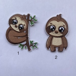 May include: Two embroidered iron-on patches featuring sloths. The first patch shows a sloth hanging on a branch with green leaves. The second patch shows a sloth standing with its arms down. Both sloths have large eyes and a brown and beige color scheme.